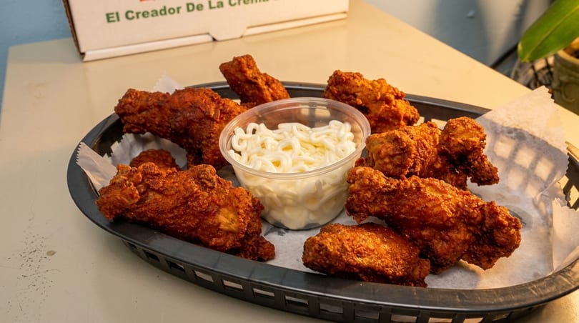 A black basket filled with crispy fried chicken pieces and a small cup of white dipping sauce.