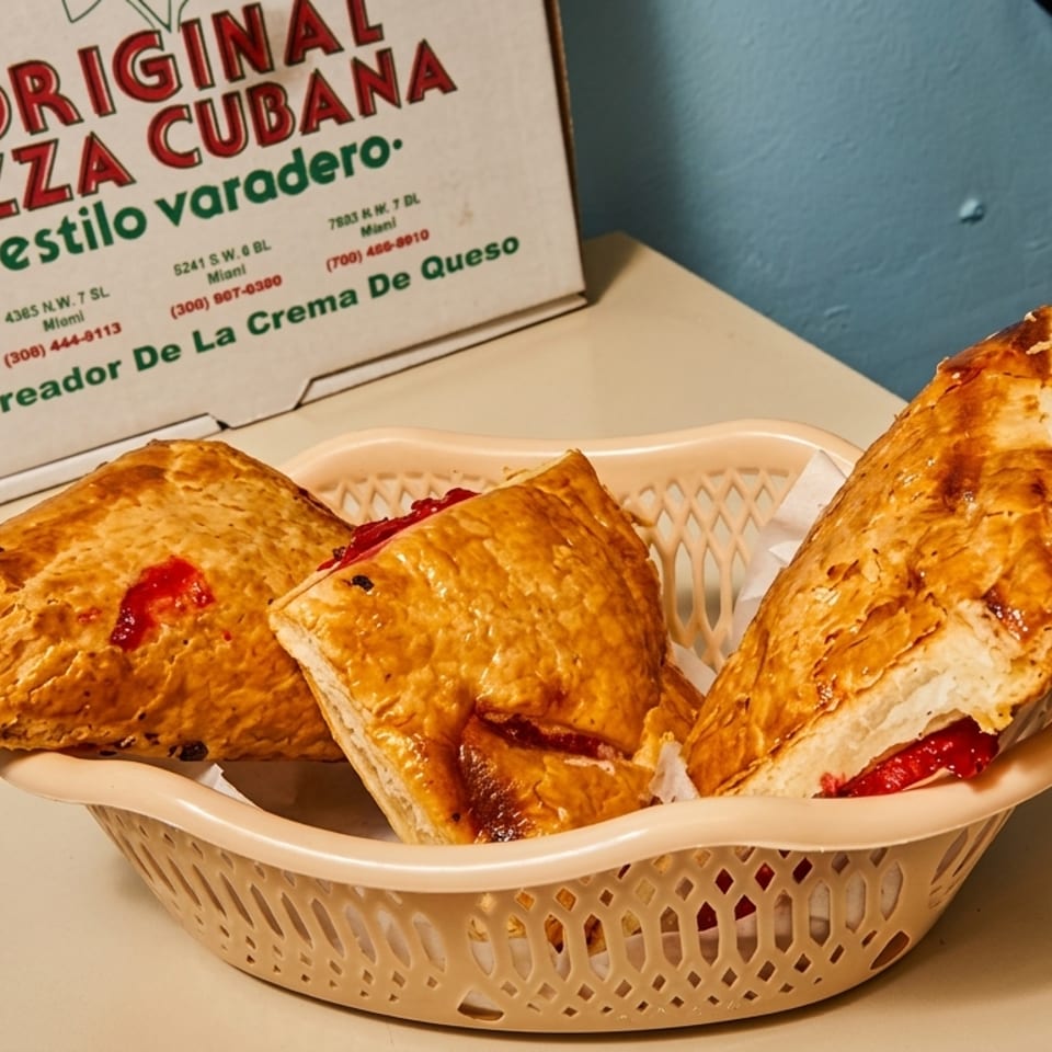 Three Cuban-style pizza pastries with red filling in a basket, with a pizza box behind them.