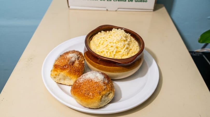 Two sugar-dusted buns and a bowl of creamy cheese dip on a white plate.
